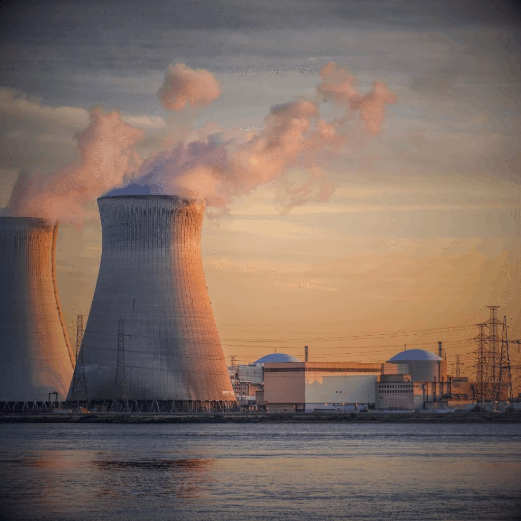 Power Generation Infrastructure: Power station with cooling towers emitting steam at sunset.